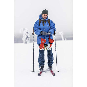 Skier wearing blue jacket and beanie holding Hestra red gloves in snowy landscape
