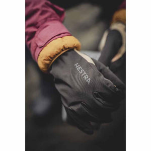 Person wearing black Hestra gloves with a maroon and yellow jacket