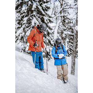 Two skiers in helmets and winter gear standing in snowy forest