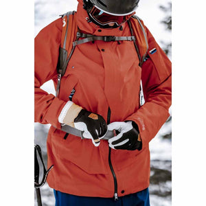 Skier wearing a red jacket and black and white Hestra gloves adjusting a backpack strap