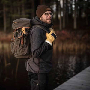 Person wearing Hestra leather gloves and a backpack standing near a forest lake
