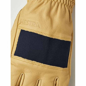 Tan leather Hestra glove with a dark blue fabric patch on the back of the hand