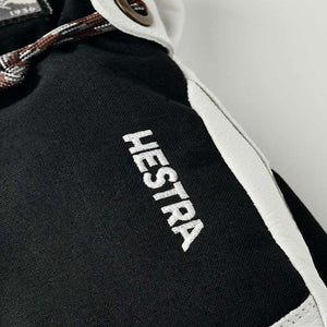 Hestra logo embroidered on black fabric with white leather trim