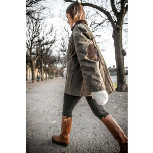 Person wearing olive green waxed jacket with elbow patches and brown leather boots walking on a path