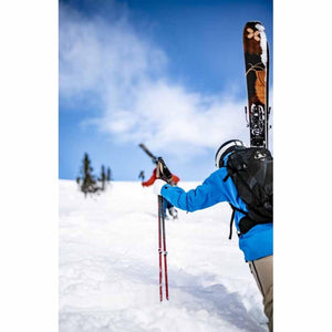 Skier wearing Hestra gloves hiking uphill with skis on backpack