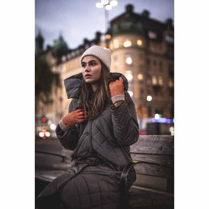 Woman wearing Hestra tan leather gloves and a winter coat sitting on a bench