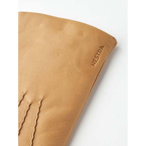 Close up of tan leather Hestra glove showing embossed logo and stitching detail
