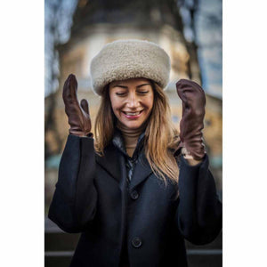 Woman wearing a beige shearling hat and brown leather gloves with a black coat