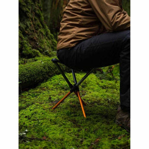 Person sitting on a Hillsound portable tripod stool in a mossy forest