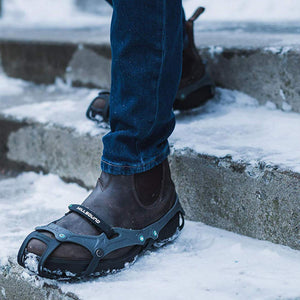 Person wearing Hillsound traction cleats over brown leather boots on snowy concrete steps