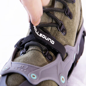 Hand pulling the Hillsound branded strap on a hiking boot equipped with traction cleats