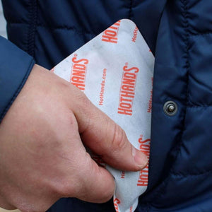 Hand placing a Hothands hand warmer packet into a blue jacket pocket