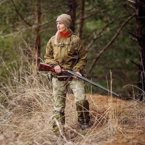 Woman in outdoor gear holding a shotgun in a forest
