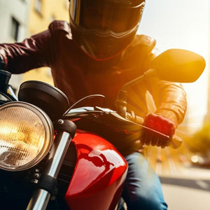Motorcyclist wearing a helmet and leather jacket riding a red motorcycle on a city street