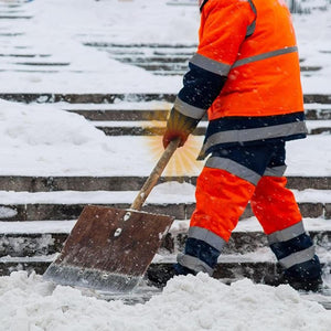 Worker in high visibility orange uniform shoveling snow from stone steps