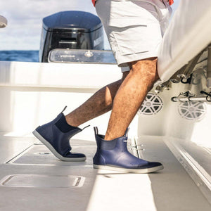 Person wearing navy blue Huk deck boots on a boat deck