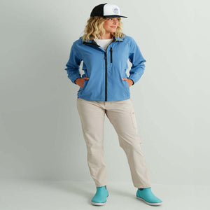 Woman wearing a blue Huk hooded jacket and beige trousers with a Huk cap