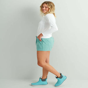 Woman wearing Huk white long sleeve shirt and teal shorts with matching teal ankle boots