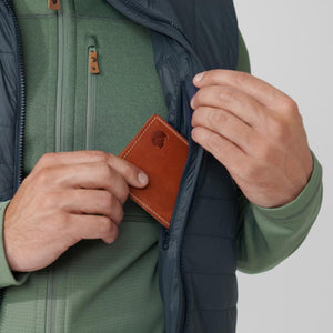 Person placing a brown leather Fjallraven wallet into the chest pocket of a green fleece vest
