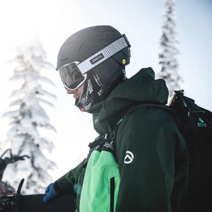 Person wearing a Smith helmet and goggles with a green jacket and backpack in a snowy forest