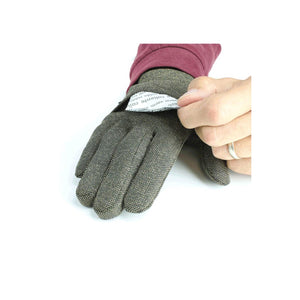 Hand inserting a small white heat pack into a pocket on a textured brown glove
