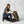 Woman kneeling beside a green Fjallraven hiking backpack wearing a cap and outdoor gear