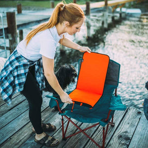 Woman placing an Ignik orange heated seat pad onto a folding camping chair on a wooden dock