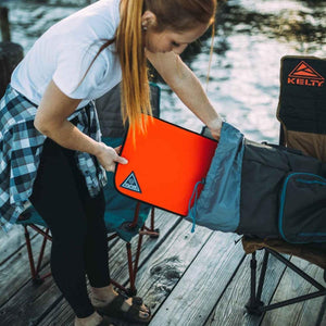 Person placing an Ignik orange fire pad into a carrying bag on a wooden dock