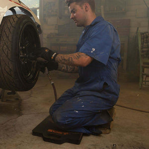 Mechanic kneeling on an Impacto mat while using a pneumatic tool on a car wheel