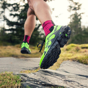 Runner wearing bright green Inov-8 trail running shoes on a rocky path