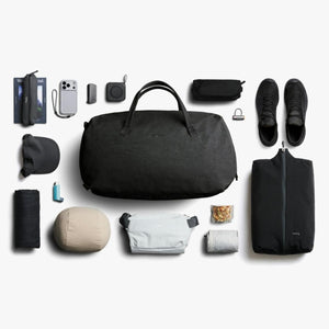 Bellroy black duffel bag surrounded by organized travel accessories and personal items on a white background