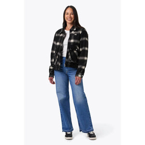 Woman wearing a Mobile Warming black and white plaid jacket over a white shirt and blue jeans