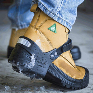 Tan work boot with a black Devisy ice cleat attachment on a snowy surface