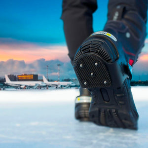 Close up of black anti slip ice cleats on boots worn on icy airport tarmac