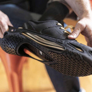 Hand stretching a black K1 Ice Cleat over the sole of a black shoe
