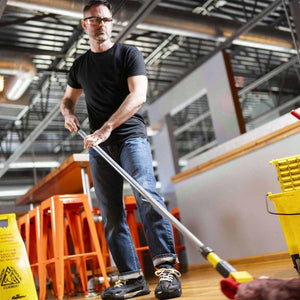 Man wearing K1 Ice Cleats mopping a floor with a caution sign nearby