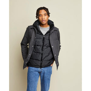 Model wearing a Kelvin black hooded puffer jacket layered under a dark grey canvas jacket with blue jeans