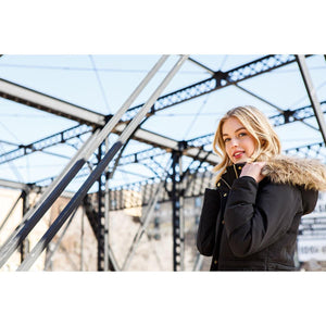 Woman wearing a black Kelvin parka with a faux fur hood on a metal bridge