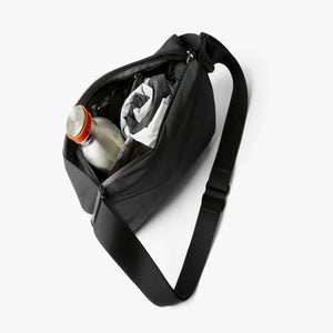 Open black Bellroy sling bag containing a metal water bottle and folded clothing