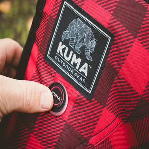 Hand pressing a Kuma Outdoor Gear power button on red and black plaid fabric
