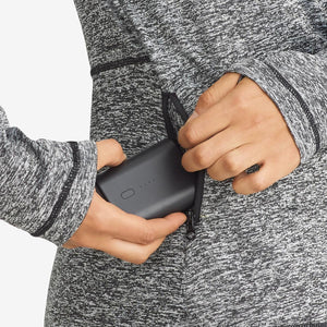 Close up of hand placing a black portable power bank into a zippered pocket of a grey marl athletic jacket