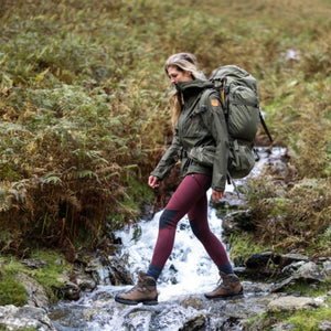 Person wearing FjallRaven jacket and backpack hiking through a shallow stream