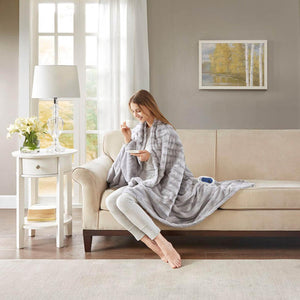 Person sitting on a sofa wrapped in a grey faux fur electric heated throw blanket