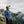 Person wearing a blue Fjallraven fleece jacket and cap standing in front of mountain peaks