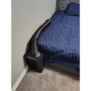 Black portable bed cooling unit with flexible air hose directed onto a blue bedspread