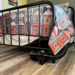 Mattress Cooler unit with black hose connected to a bed frame with a patterned quilt