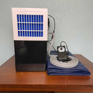 Black and white water cooling unit with a blue mattress pad and power adapter on a wooden surface