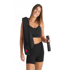Woman wearing MiHigh black activewear holding a black towel and remote