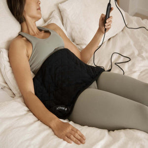 Person lying in bed using a black MiHigh infrared heating pad with a handheld controller