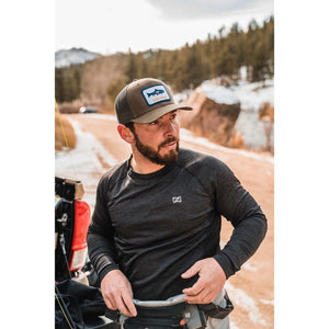 Man wearing a Yakoda trucker hat and black long sleeve shirt standing by a truck